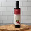 Italian Raspberry Balsamic Vinegar is shown, standing alone, on an olivewood board in a white tile kitchen