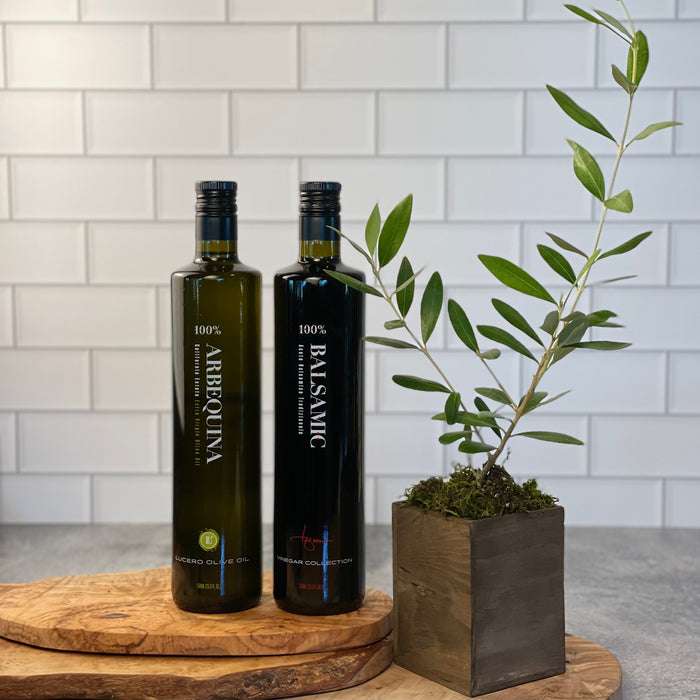 Large bottles of Arbequina and Balsamic Vinegar are shown with a live olive tree.