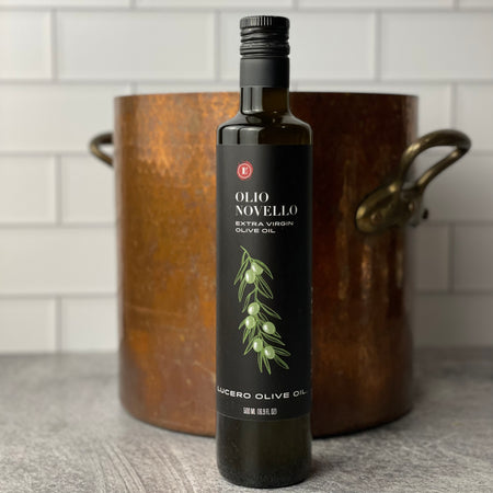 A single bottle of Olio Novello is placed in front of a hand hammered copper stock pot.