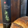 Close up of Olio Novello bottle shown next to a crusty loaf of artisan bread