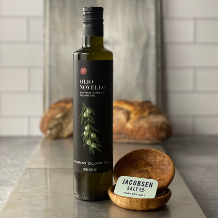 A bottle of Olio Novello is shown with two mini olivewood dipping bowls  and a small "slider tin" of Jacobsen's Kosher Sea Salt