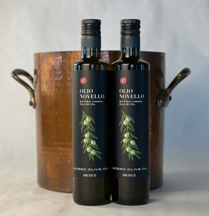 two bottles of Olio Novello are placed side by side in front of a hand hammered copper stock pot.