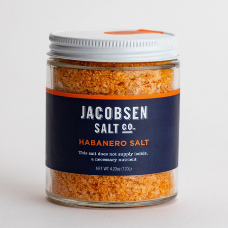 The coarse and bright orange salt crystals show boldly through the clear glass jar of Jacobsen's Habanero Salt, shown in close up on a white background.