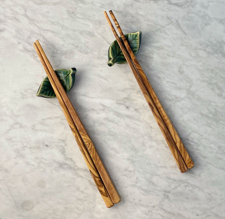 Two pairs of olivewood chopsticks (4 pieces) are shown resting on ceramic chopstick holders shaped like green leaves.
