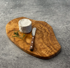 Small 12" olivewood board is shown with a small round of brie and rosewood handled spreader.