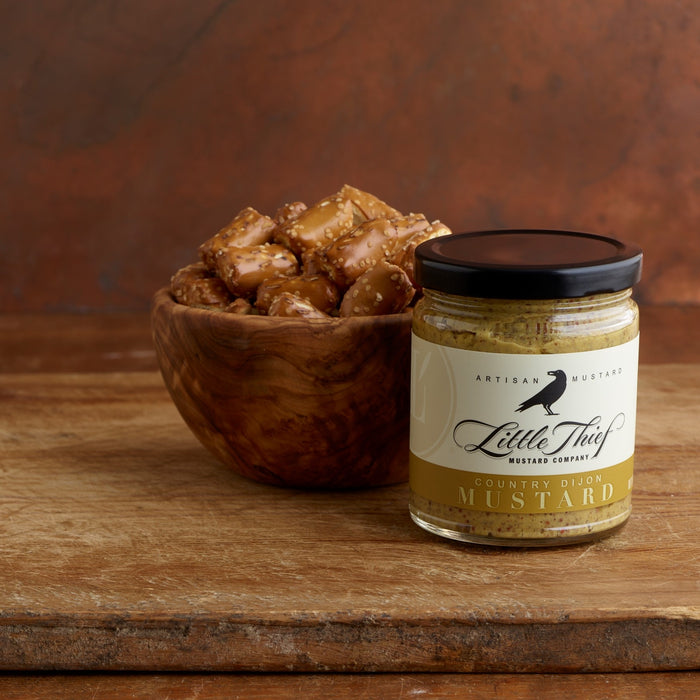 A small olivewood bowl filled with thick pretzels wiht a jar of mustard in the foreground.