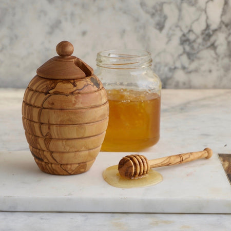 Olivewood honey pot is shaped like an old-fashioned English straw bee skep. Removable lid has a cut out for the accompanying honey dipper, whimsically shaped like a beehive on a stick.